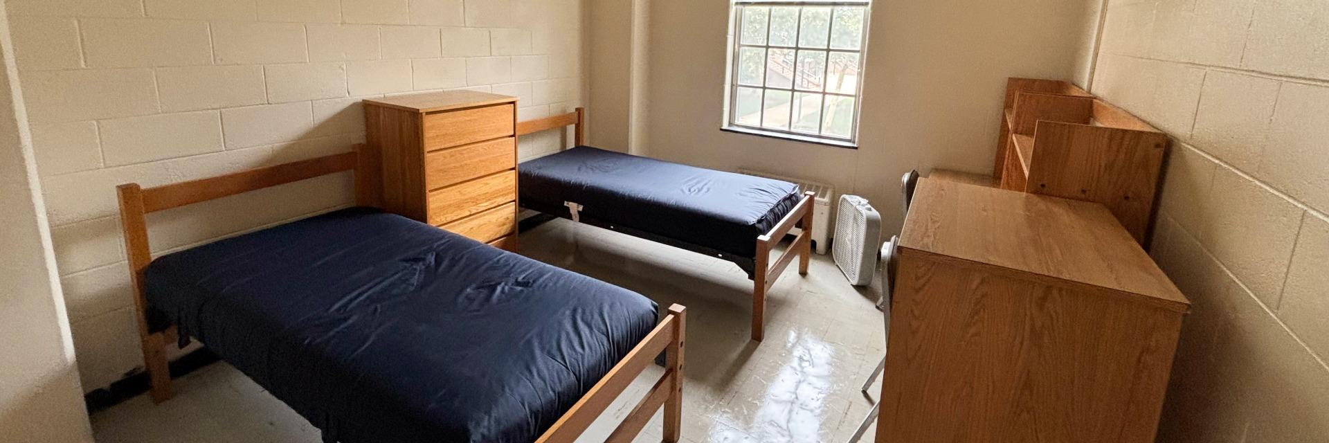 A furnished residence hall double room with two twin beds, two desks, a dresser and a window..