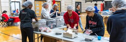 Six University of Maryland Students wearing hair nets package food for the Terps Against Hunger food packaging event in Ritchie Coliseum.